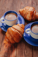 two cups of coffee and croissants on a wooden background, good light, morning atmosphere