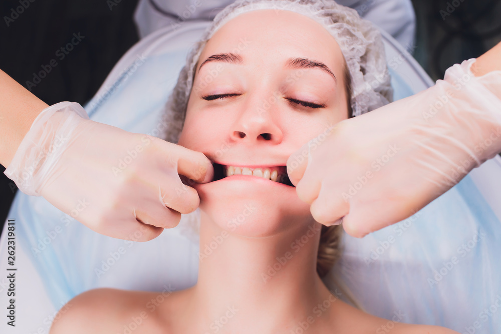 Wall mural cosmetologist makes a buccal massage of the patient's facial muscles.