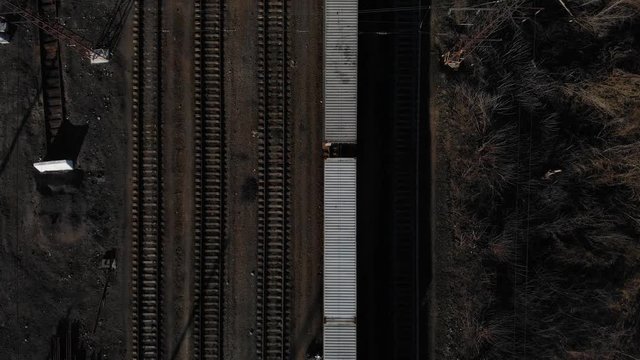 Aerial view of a large train on the rails next to the river. The camera flies over a long train of tanks standing on the rails