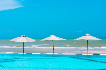 Umbrella and chair around swimming pool neary sea ocean beach with blue sky and white cloud