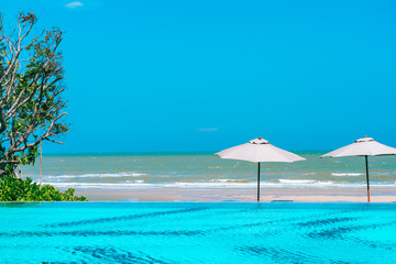 Umbrella and chair around swimming pool neary sea ocean beach with blue sky and white cloud