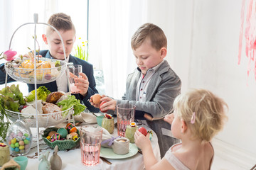 Brothers and sister enjoying Easter breakfast with their pet rabbit playing on the table. 