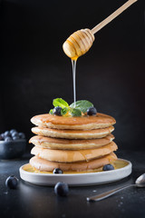 Sweet homemade stack of pancakes with fresh blueberry, honey and mint in modern plate on black.