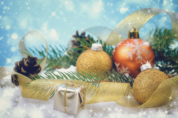 Christmas balls, small box with gifts, festive ribbon and fir branches on the snow over a shiny blue background. Selective focus. Festive Happy New Year card.