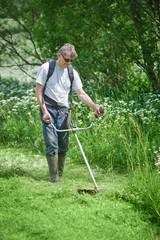 European man is mowing the lawn on his countryside plot.