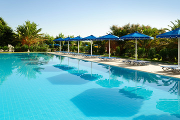 Sunbeds with umbrellas and palm trees around the pool, Greece.