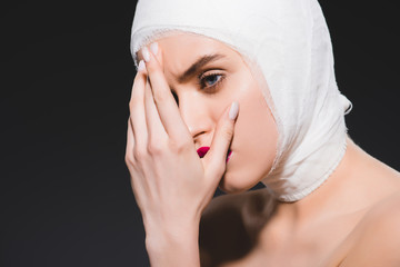 young woman with bandaged head covering face isolated on grey