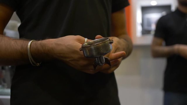 Male barista in a black t-shirt with a metal tempera for coffee. On his right hand is a silver bracelet. Making coffee. The work of baristas.