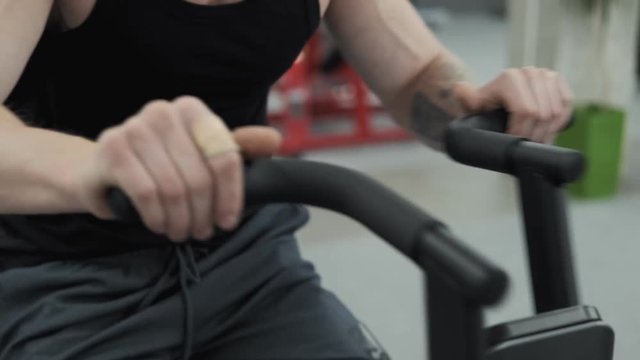 Close up of man working out on exercise bike at gym in slow motion. Muscular man using spinning bicycle