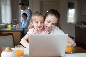 Mother and daughter playing computer while father and son cooking