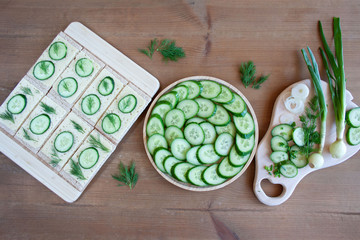  Light, spring sandwiches with cheese, fresh cucumber and dill, next to a tray with slices of cucumber and a board full of green spring vegetables