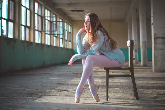 Photo of ballerina while she’s sitting on the chair in an old building. Young, elegant, graceful woman ballet dancer