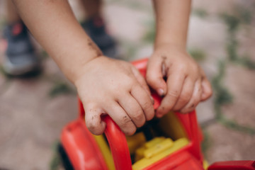 A little girl plays with a tractor in the street. A child gets dirty in the ground.