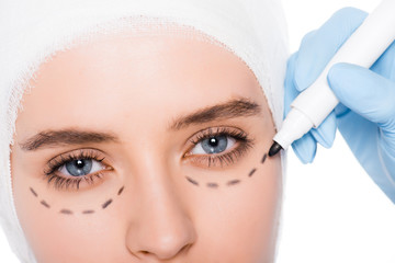 cropped view of plastic surgeon in latex glove holding marker pen near girl with marks on face isolated on white