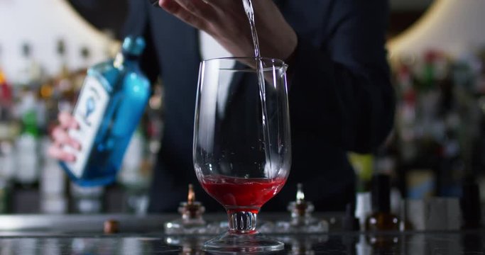 Bartender pouring gin into the mixing glass to prepare a negroni cocktail. Close up shot on 6k RED camera.