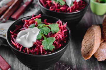 Thinly sliced ​​fresh beets in a black salad bowl with sprigs of cilantro ready for eating are on a wooden table. Thinly shredded beet salad..