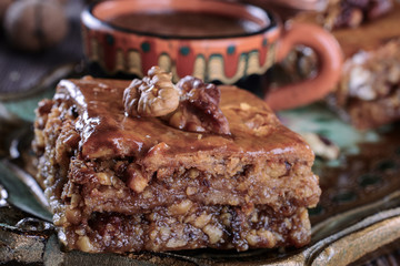 Baklava cake with nut on top next to blured cup of  coffee on a  wooden vintage tray, macro.