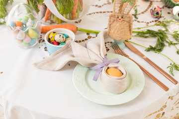 Table set with a painted egg wrapped in a linen napkin shaped like bunny ears on Easter breakfast table. Polish Easter