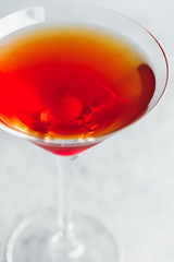 Manhattan cocktail with bourbon and maraschino cherry garnish on a white table.