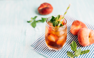 The glass of peach ice tea on wooden table. Cuba Libre or long island iced tea cocktail, cold drink or lemonade with fruits and mint