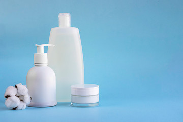 Three white plastic mockup bottles for shampoo or shower gel, dispenser and glass small tube for cream and cotton flower on lighnt blue empty background with copy space