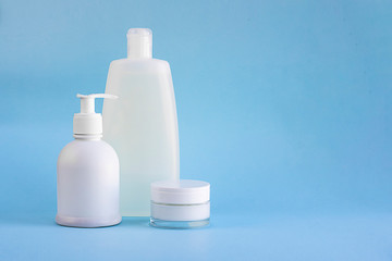 Three white plastic mockup bottles for shampoo or shower gel, dispenser and glass small tube for cream on lighnt blue empty background with copy space