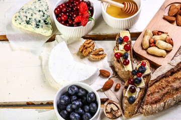 Toast crostini with fresh berries blueberry and cheese, thyme and hazelnuts, over white wooden textured board. Top view, copy space