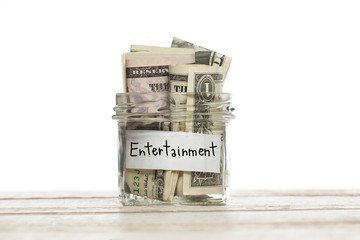 US dollar money for entertainment in saving glass jar on wooden table against white background