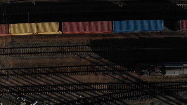 Aerial view of a large train on the rails next to the river. The camera flies over a long train of tanks standing on the rails