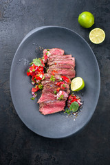 Traditional South American barbecue wagyu roast beef sliced with pico de gallo and salsa verde garnished as top view in a modern design plate