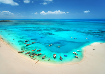 Aerial view of the fishing boats on tropical sea coast with sandy beach at sunny day. Summer holiday. Indian Ocean, Zanzibar, Africa. Landscape with boat, white sand, azure water, blue sky. Top view - obrazy, fototapety, plakaty