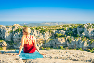 Yoga Fitness Woman Resting and Enjoying View after Training Session. Sitting at the Edge of Cliff Overlooking Mountain Range and Ocean in Far Distance.