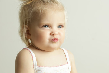 Studio portrait of an adorable blonde baby girl with an angry facial expression 