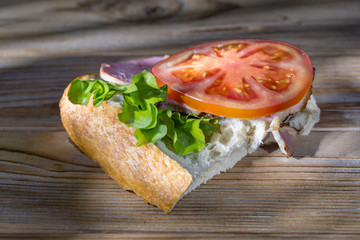 Close up view of a ham and lettuce and tomato sandwich on wooden background illuminated by spotty sunny light. Soft focus.