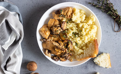 Chicken breast in cream sauce with mushroom, onion and thyme served with couscous in a white plate.
