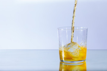 Whiskey runs into a glass of ice and whirls around, against a neutral background and floor reflection