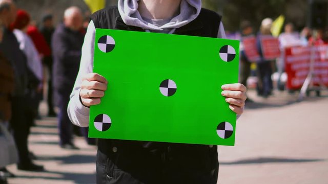 Man near people on strike standing hold greenscreen banner. Empty poster with tracking points in person's hands. Demonstration in middle of day. Serious and sad guy with clear placard for copyspace 4k