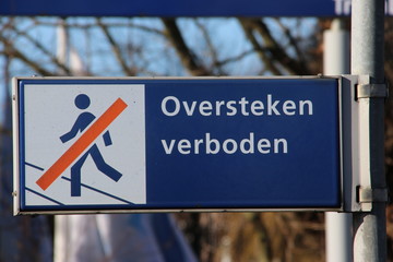 Blue and white sign with dutch language text "oversteken verboden" which means that trespassing the rails is not allowed