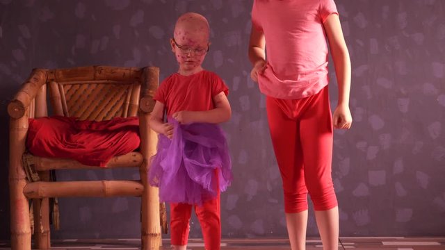 Two funny blond children with red ball are playing in room in pink clothes