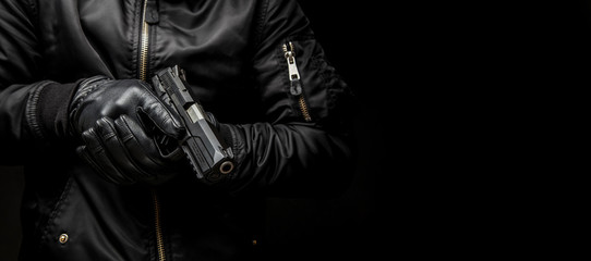 Fototapeta na wymiar a man in a black jacket and black gloves holding a gun on a dark back