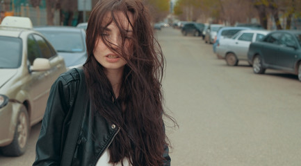Fototapeta na wymiar Girl in windy day with blowsy hair in the street with parked cars