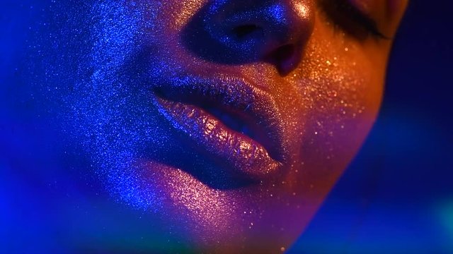 Beautiful sexy lips, kiss. Fashion model woman kiss lips in bright sparkles, colorful neon lights. Trendy glowing gold skin makeup. Slow Motion 4K UHD video footage. 3840X2160
