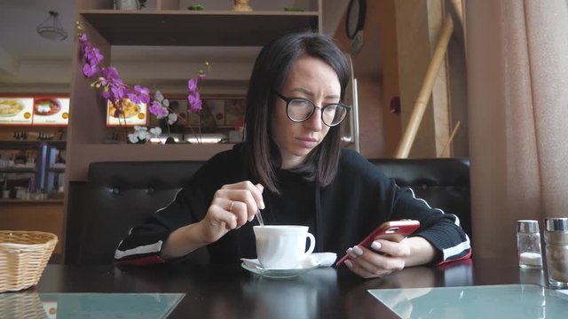 Young wonam use mobile phone while sitting in comfortable coffee shop during work break, charming happy female reading fashion news on cell telephone during breakfast in restaurant.