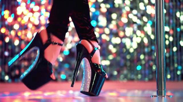 Young sexy striptease dancer moving in high heels shoes with rhinestones on stage with pylone in strip night club, Pole dancing. Shining background. Dance, sex, temptation concept