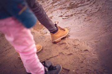 cute children of 7-8 years old, curly-haired girl and boy in a coat in the early spring by the river, touch some water with their feet