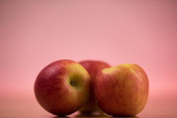 close up of tree apples with a red pink background and illuminated by studio light