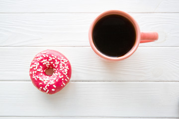 Fototapeta na wymiar A cup of black coffee and sparkling pink doughnut on white wooden table baclground. Space for text, copy space. 