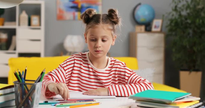 Caucasian small and cute schoolgirl drawing and coloring a picture in her room as doing homework.