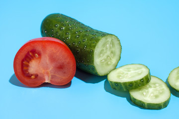 Ripe green cucumber and red tomato on blue background. Healthy eating and dieting concept.