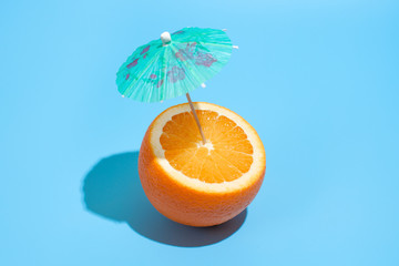 Fresh juicy orange with a cocktail umbrella isolated on blue background. Concept of Healthy eating and dieting. Drink concept